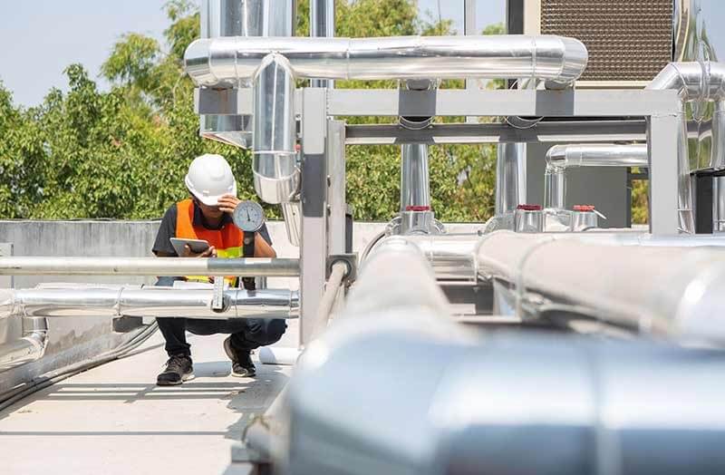 Technician reading pressure gauge on rooftop piping for air quality systems in Wilmington, NC