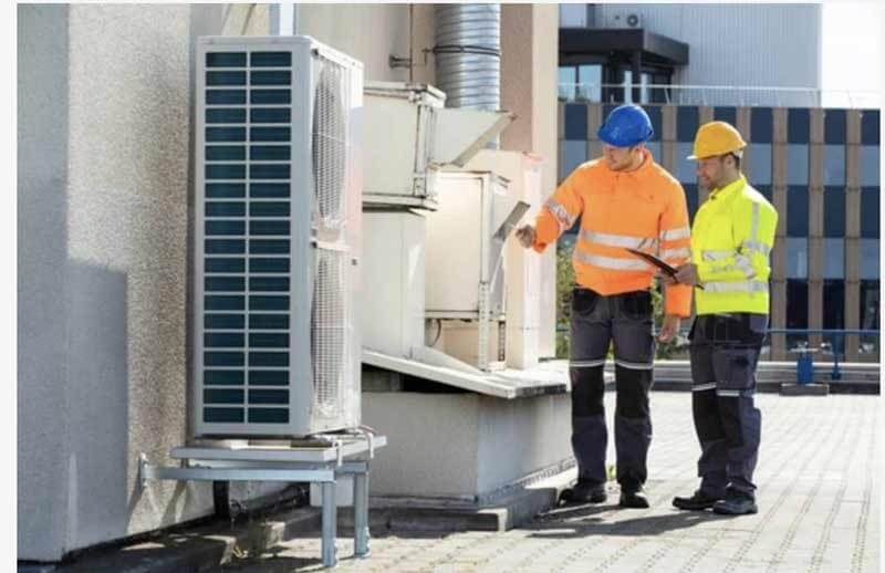 Two technicians reviewing rooftop condenser unit during commercial chiller service in Wilmington, NC