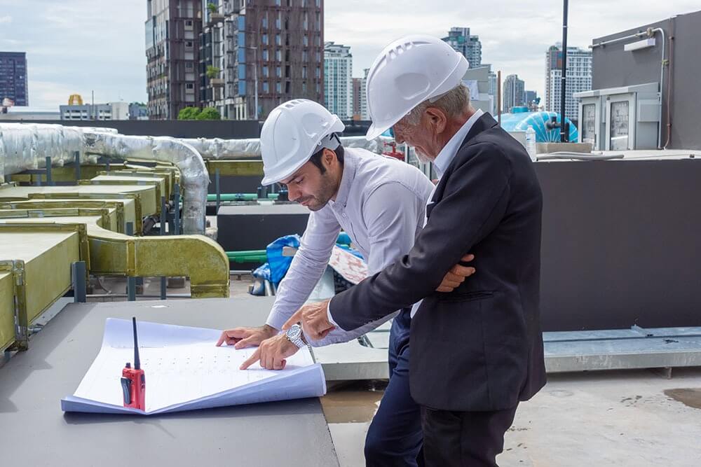 Engineer and client reviewing HVAC design plans on rooftop for Greensboro HVAC engineering company