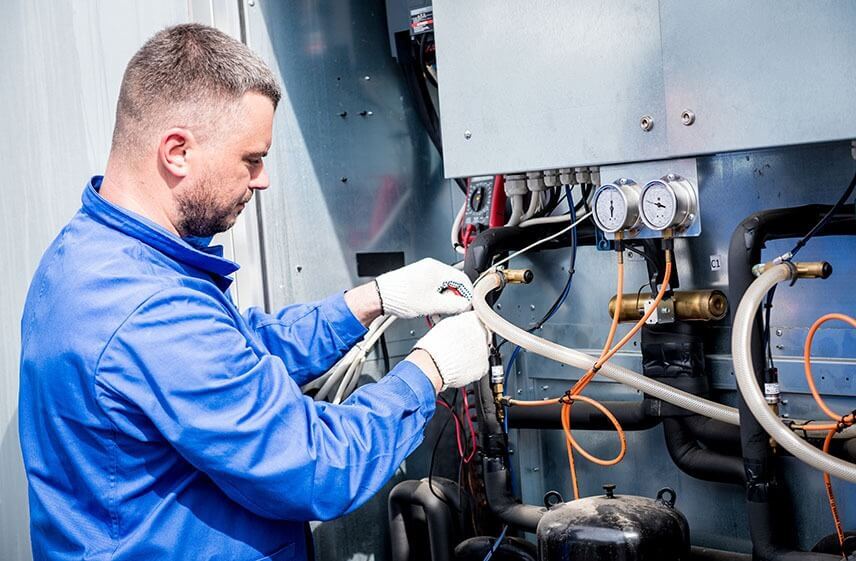 Technician servicing refrigerant lines and pressure gauges on industrial HVAC system unit