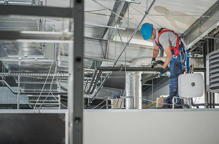 Technician performing routine commercial air conditioner maintenance on insulated ductwork system