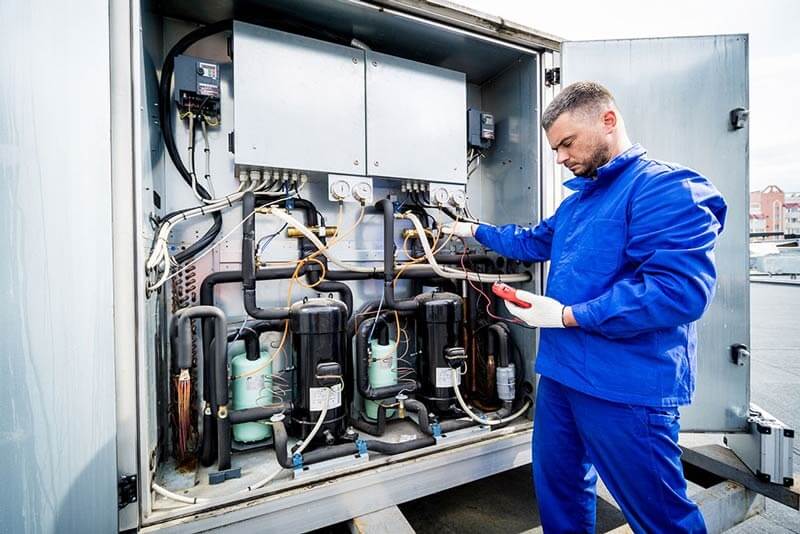 Technician testing compressor bank with multimeter as part of commercial HVAC company services